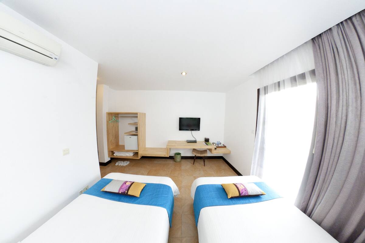 Habitación de hotel con dos camas, un escritorio, un televisor y una ventana con cortinas.