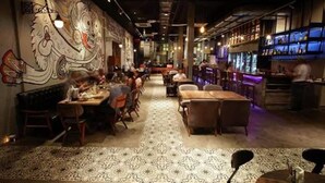 A restaurant with a long counter, patterned floor, and a mural on the wall.