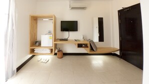 A modern hotel room with a wooden wardrobe, a flat-screen TV, a desk with a computer, a black door, and a tiled floor.