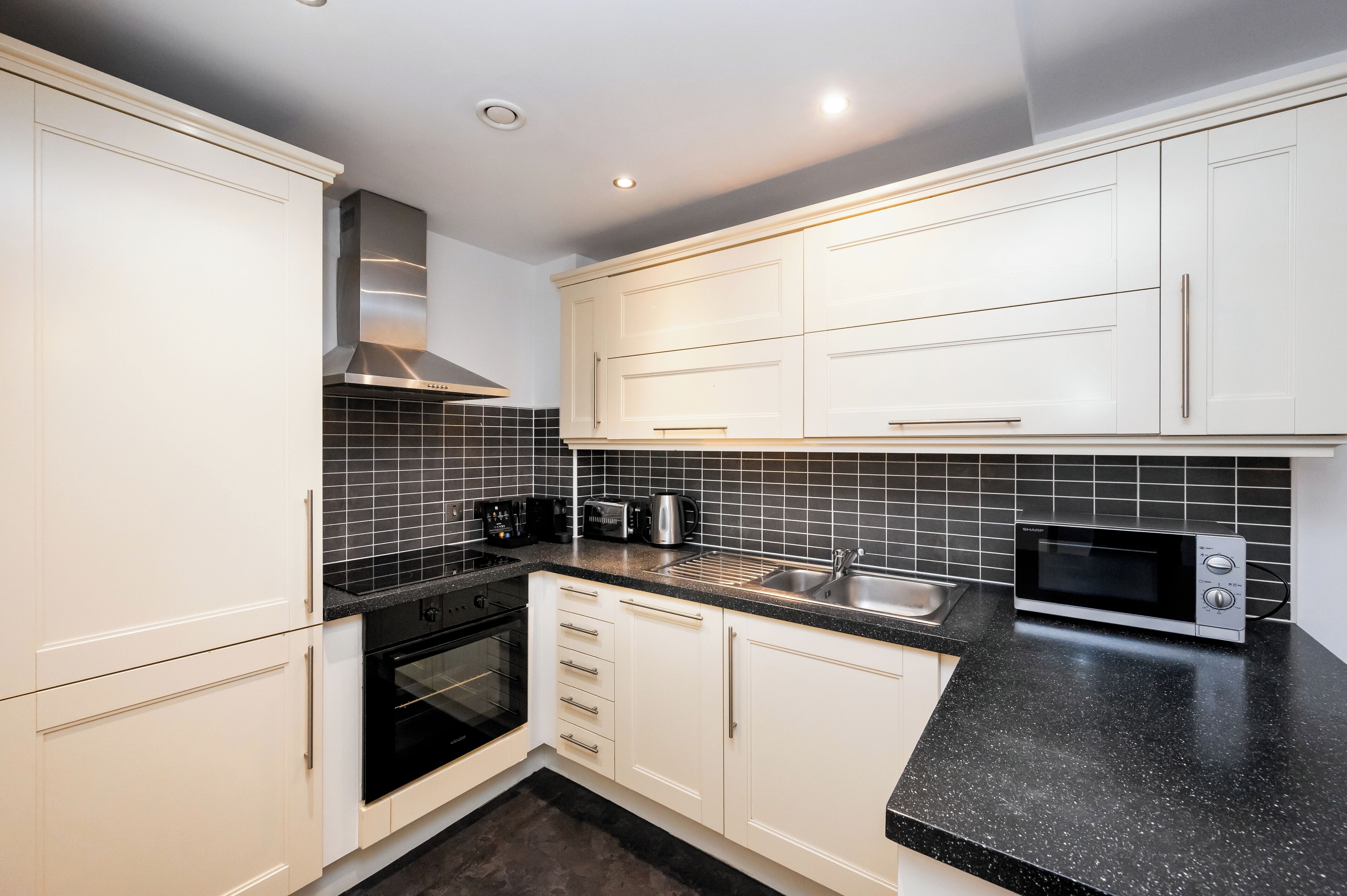 A modern kitchen with white cabinets, black countertops, a stainless steel range hood, a microwave, and a toaster.