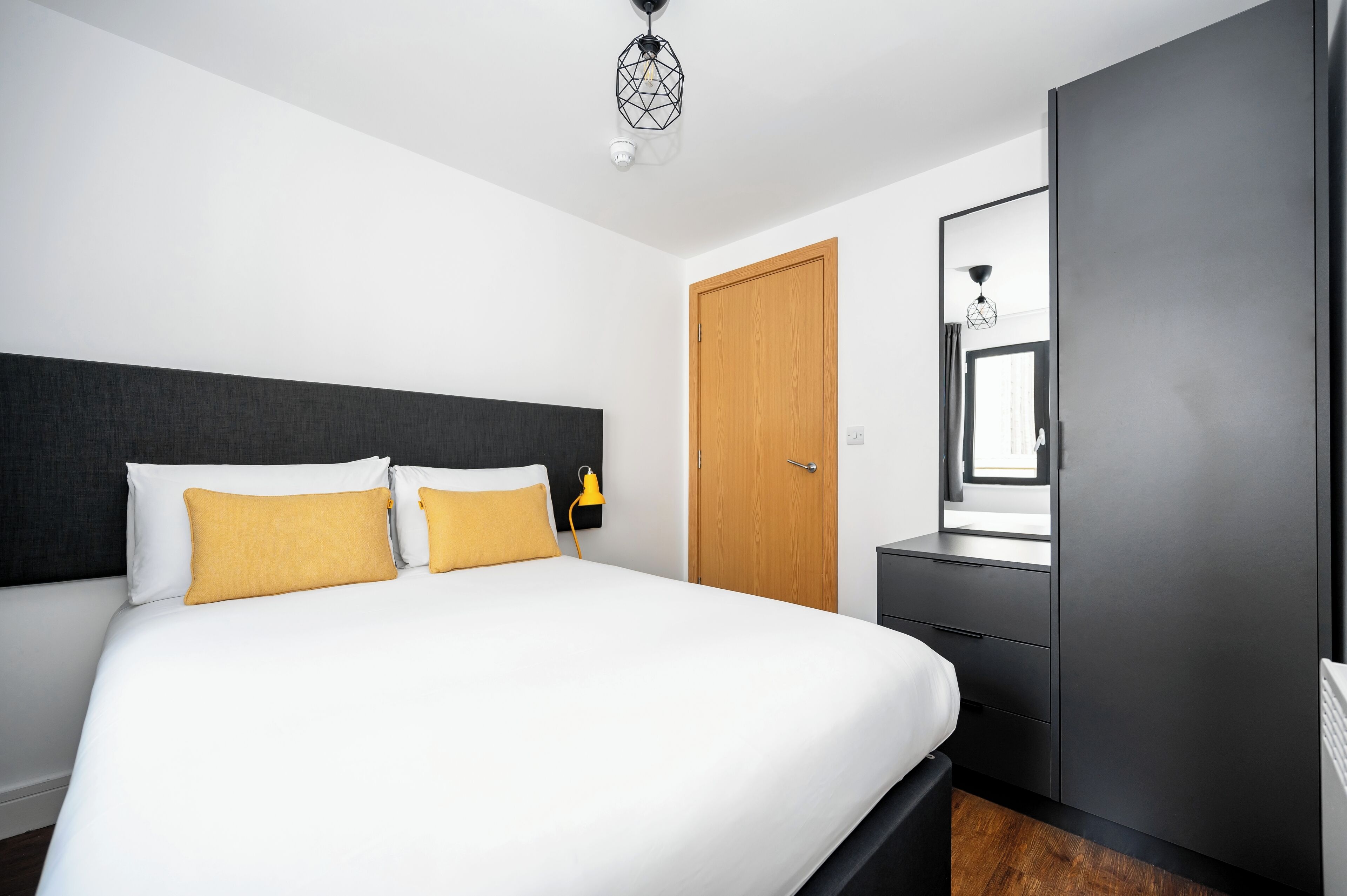 A modern hotel room with a large bed, a wardrobe, a bedside table, and a mirror.