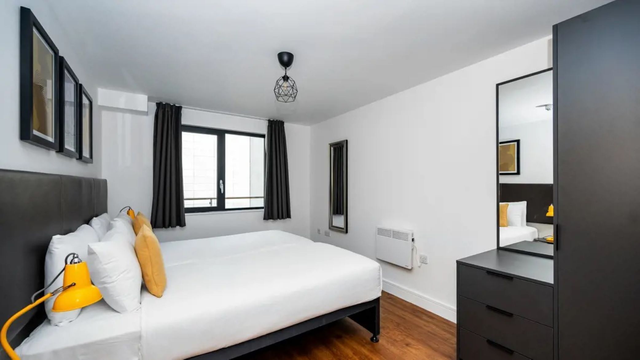 Una habitación de hotel moderna con una cama grande, una mesita de noche, un aparador y una ventana con cortinas.