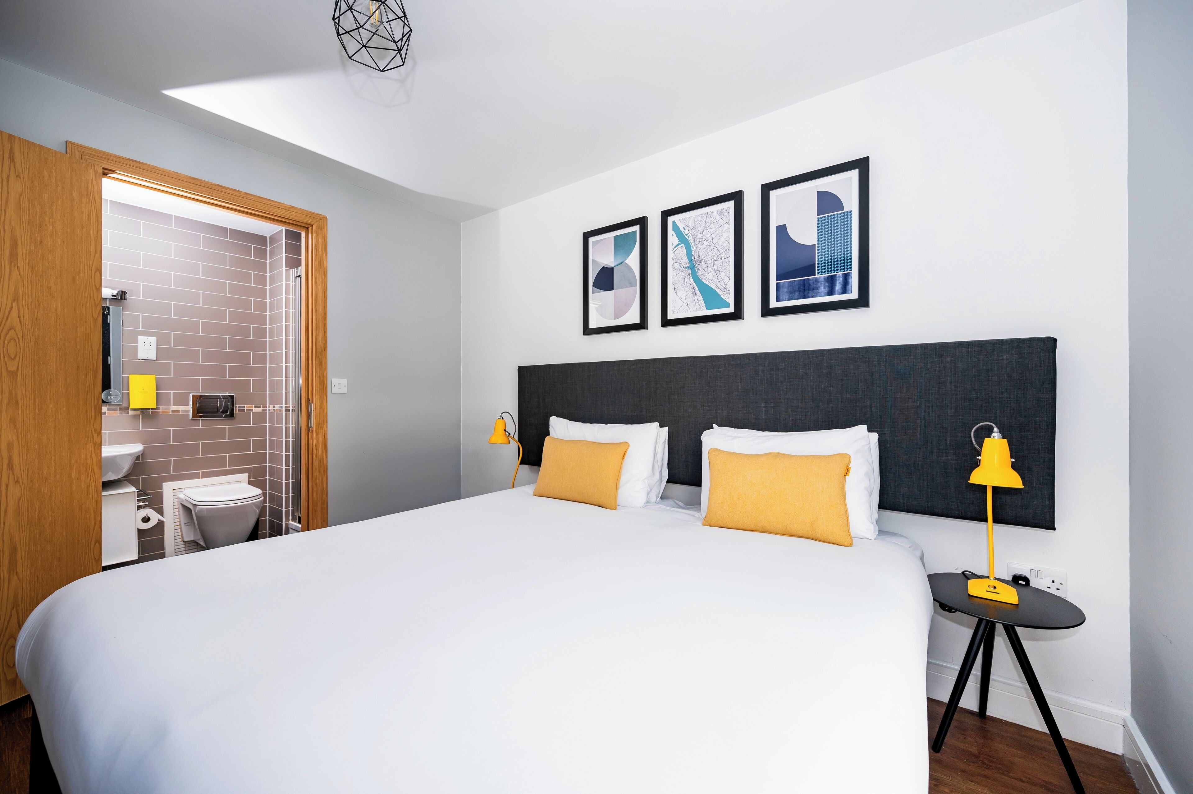 A hotel room with a large bed, two bedside tables, a nightstand, a bathroom with a sink and toilet, and three framed pictures on the wall.