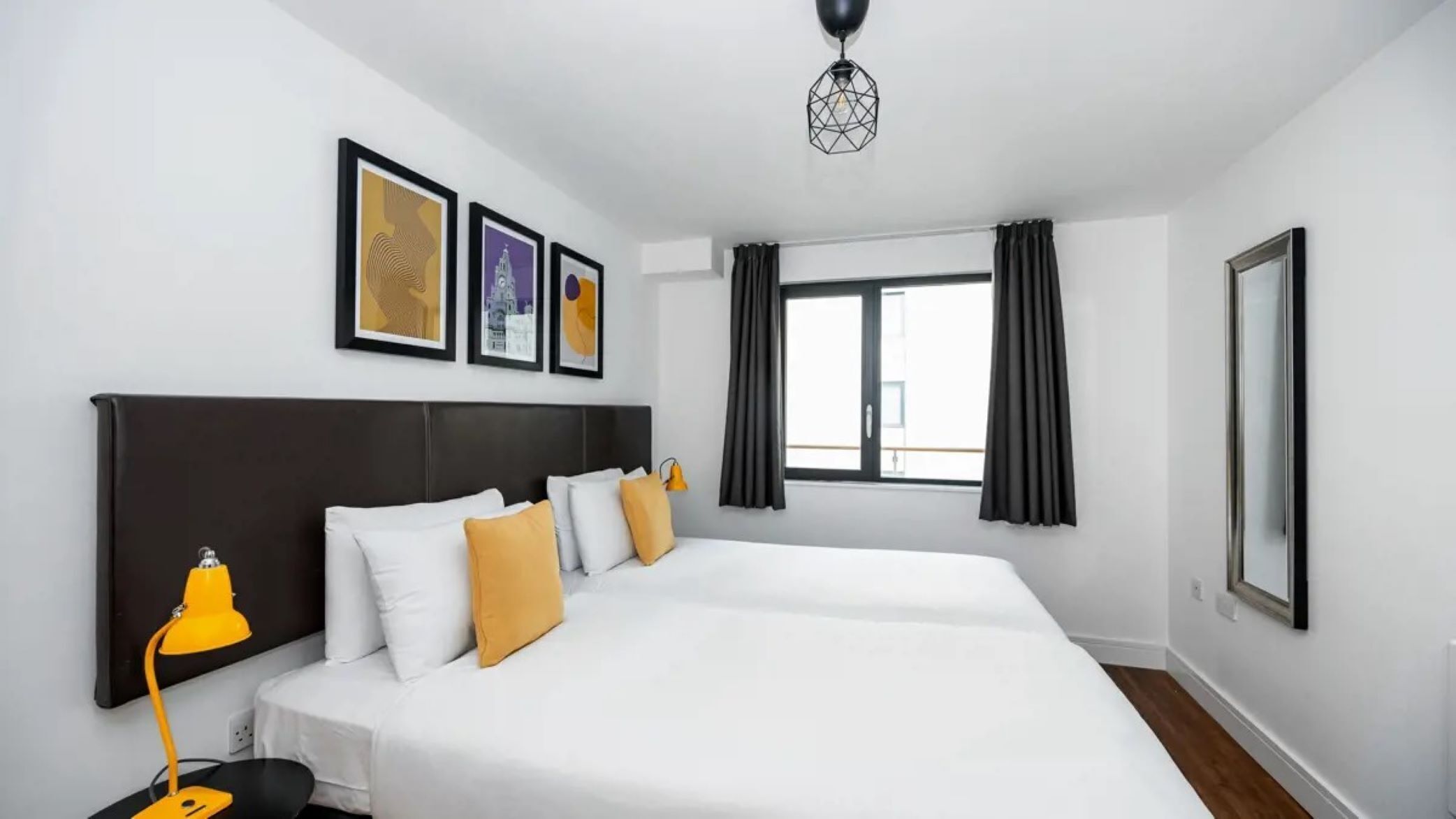 Una habitación de hotel moderna con una cama grande, un escritorio con una silla, una lámpara de escritorio y una ventana con cortinas.