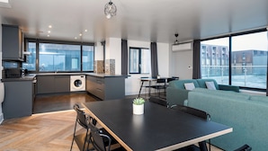 A modern kitchen with a built-in washing machine, a dining area with a table and chairs, and a seating area with a sofa and a view of the water. - Staycity Aparthotels, Liverpool, City Centre (Liverpool)