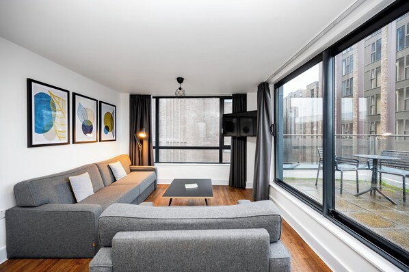 A modern living room with a grey sectional sofa, a black coffee table, and framed artwork on the wall.