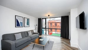 A modern living room with a grey sofa, a black coffee table, and a large window with a view of a red building. - Staycity Aparthotels, Liverpool, City Centre (Liverpool)