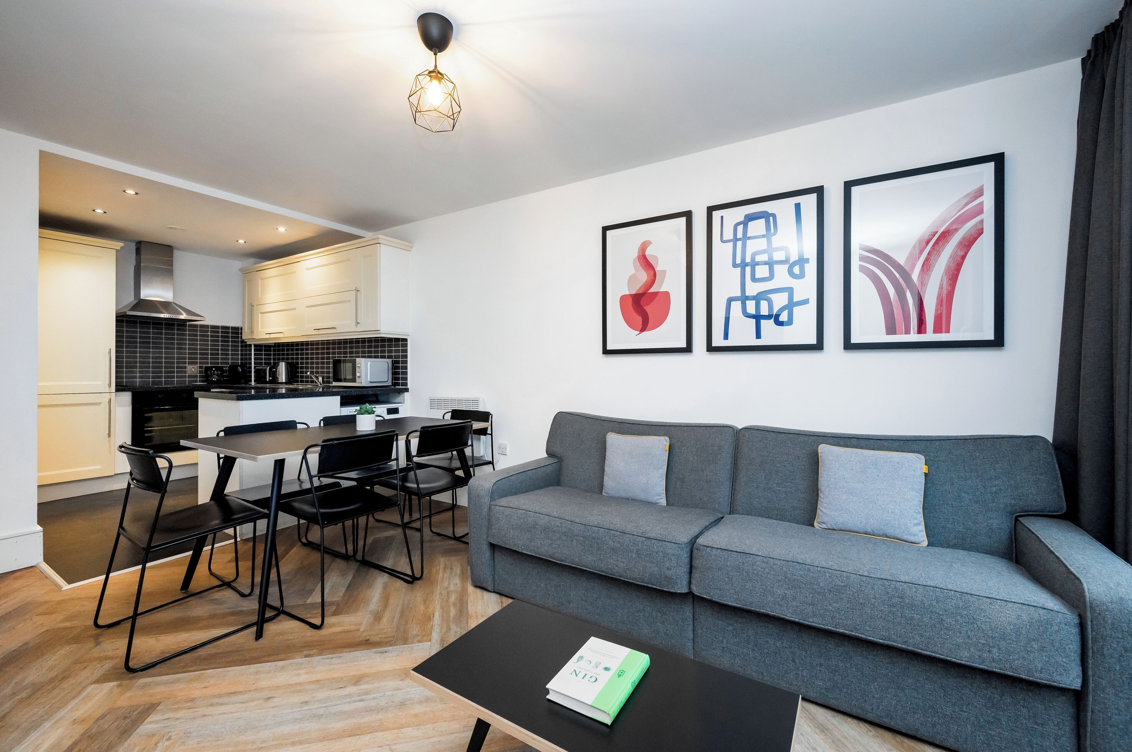 A modern living room with a grey sofa, a coffee table with a book, and a dining area with chairs and a table.