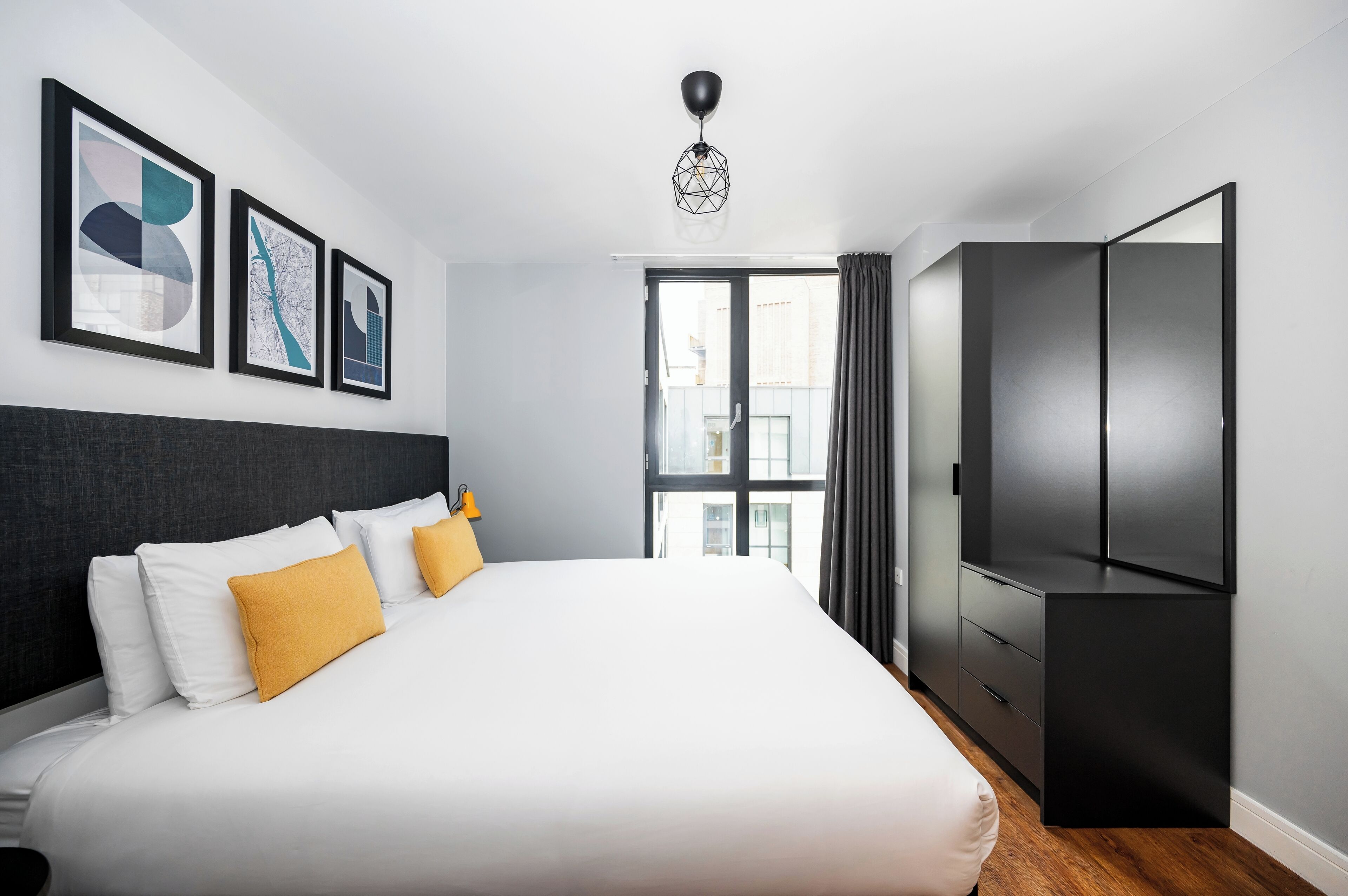 Una habitación de hotel moderna con una cama grande, un armario y obras de arte en la pared.