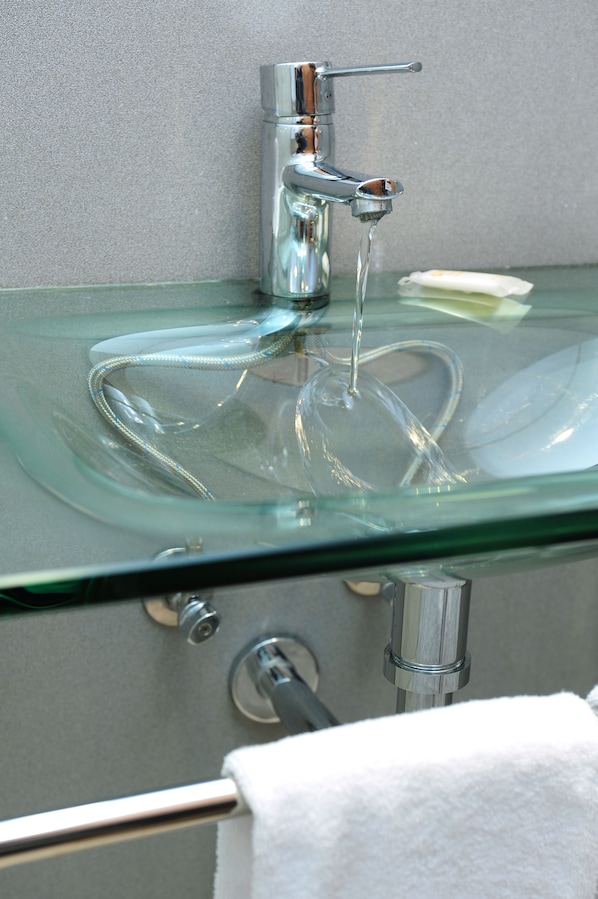 Un lavabo de vidrio transparente con agua corriendo, un perchero y un jabonera.
