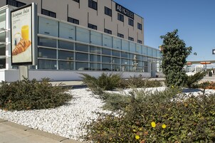 Un hotel moderno con fachada de vidrio, un cartel anunciando Desapino Dolce y un jardín bien cuidado.