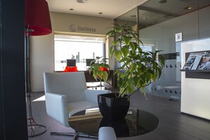Un espacio de oficina moderno con un separador de vidrio, un sofá blanco, una mesa negra y una planta en maceta.