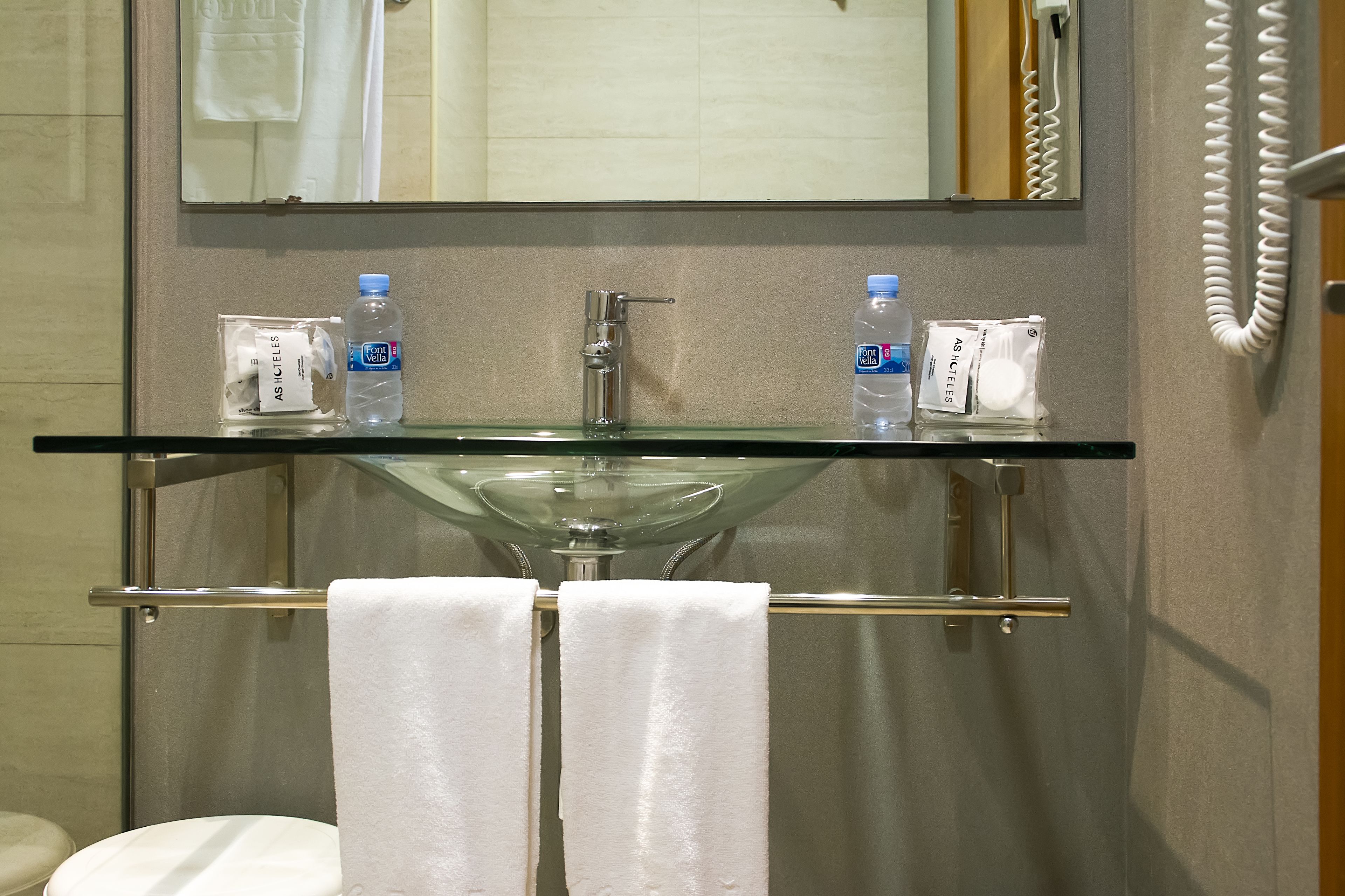 Een badkamer met een glazen wastafel, twee handdoeken en toiletartikelen op het aanrecht.