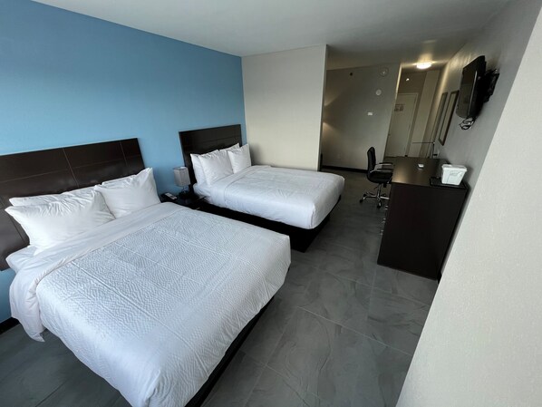 Ein Hotelzimmer mit zwei Betten, einem Schreibtisch, einem Stuhl und einem an der Wand befestigten Fernseher.