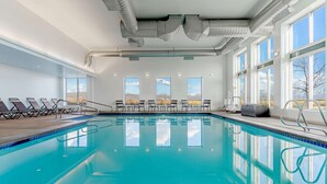 An indoor swimming pool with clear blue water, sunlit windows, and lounge chairs along the poolside. - Hyatt Place Salt Lake City Airport (Salt Lake City)