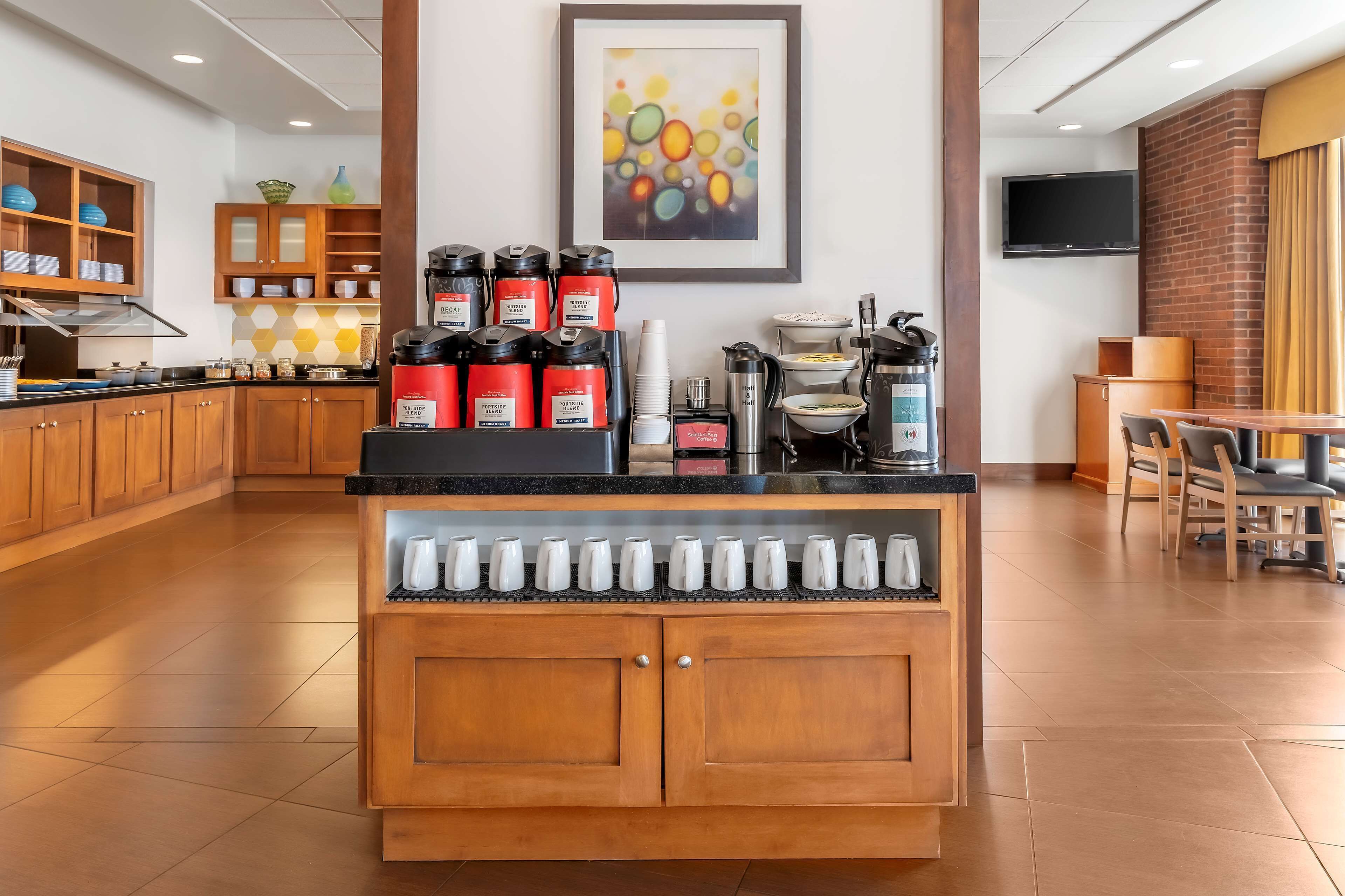 A hotel kitchen with wooden cabinets, a coffee station, and a framed abstract painting on the wall.