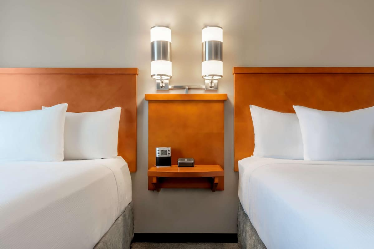 A hotel room with two beds, a nightstand with a radio, and wall-mounted lights.