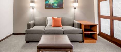 Una sala de estar moderna con un sofá gris, un cojín naranja, un banco de madera y dos lámparas fijadas a la pared.
