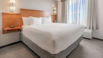 Una cama grande con cabecera de madera, dos mesitas de noche con lámparas, un ventanal con cortinas y suelo alfombrado.