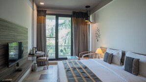 Habitación de hotel con cama, televisor, escritorio con silla, balcón con cortinas y lámpara.