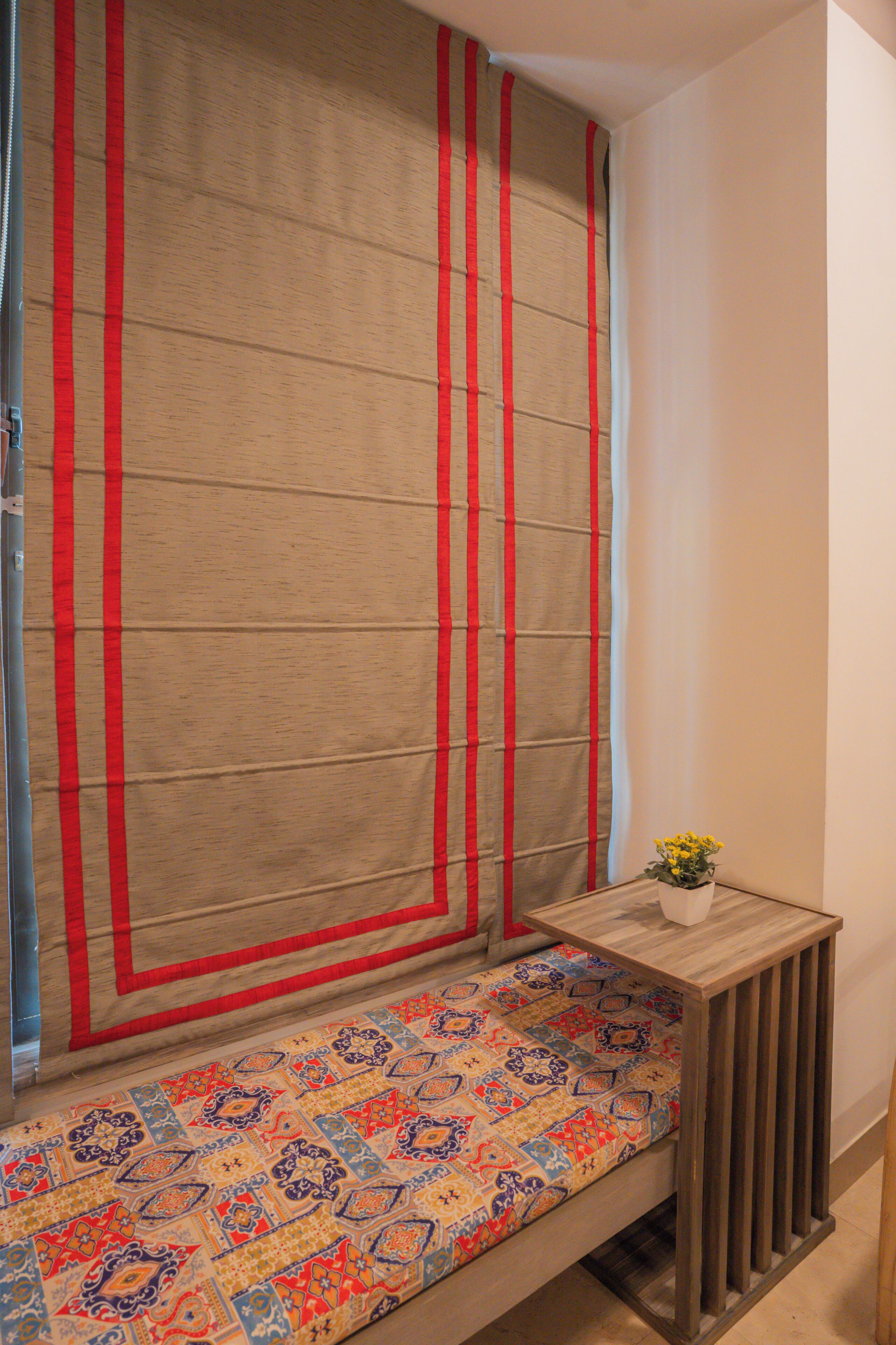 Una habitación con un banco, una mesita con un florero y una cortina con rayas rojas.