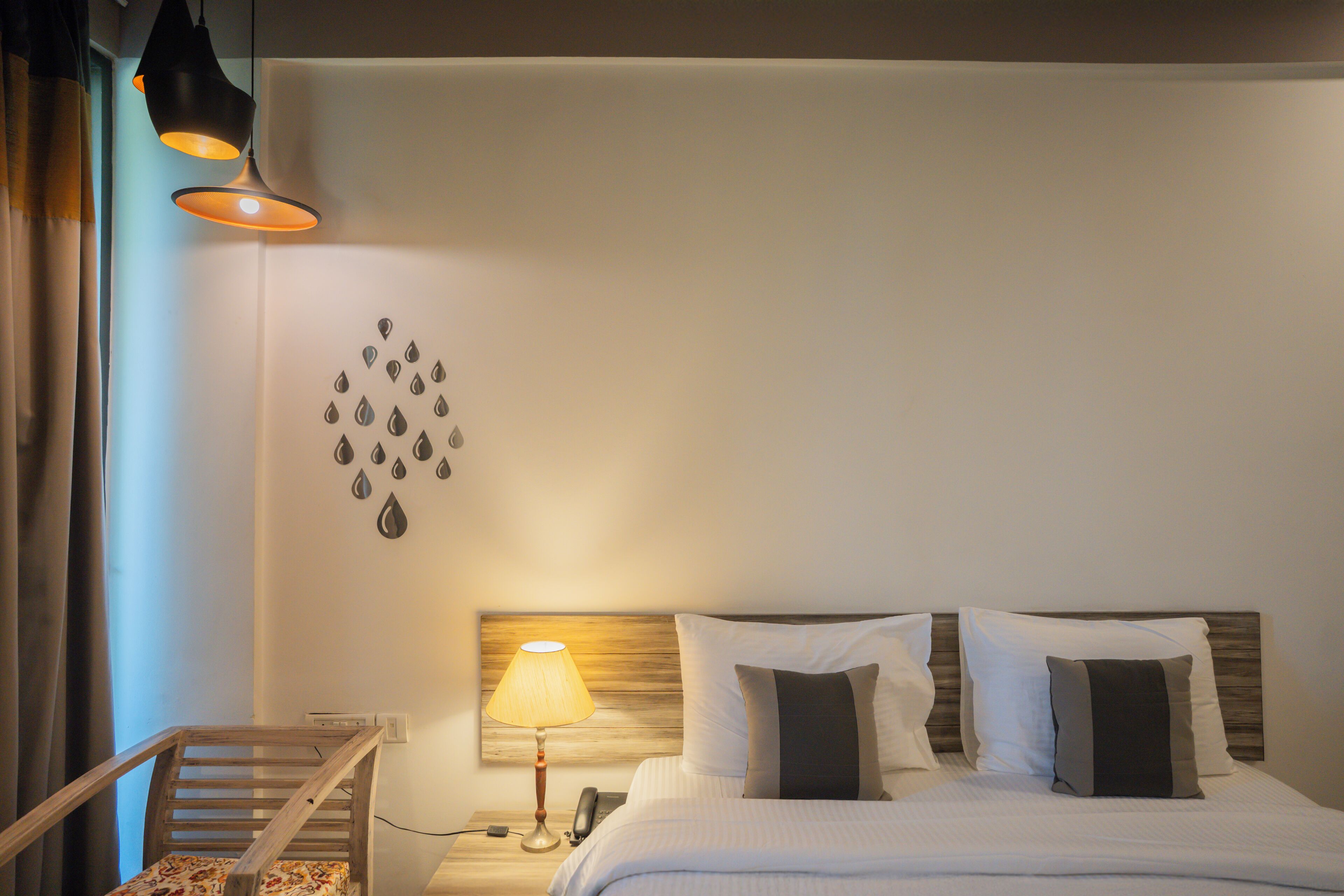 A neatly made bed with white linens and two pillows, a bedside lamp, a wooden nightstand, and a wall decoration of water droplets.