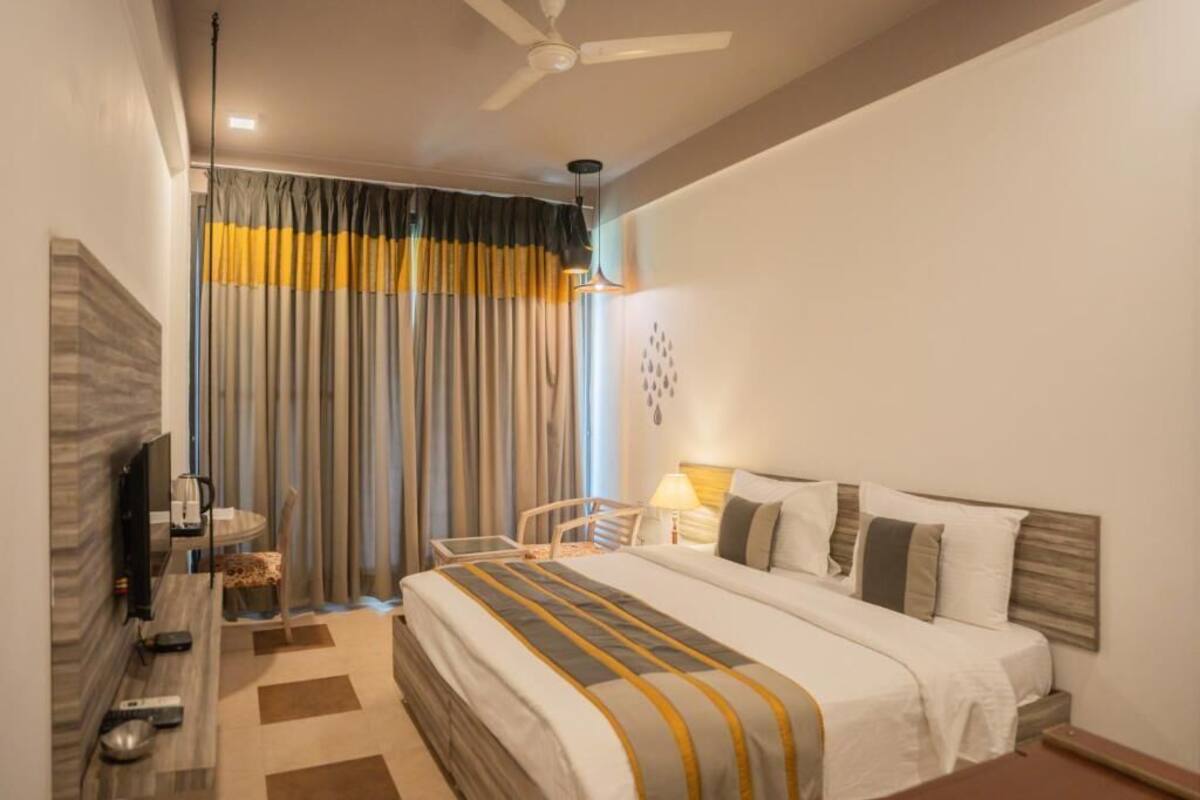 Habitación de hotel con cama, escritorio, silla, televisión y ventilador de techo.