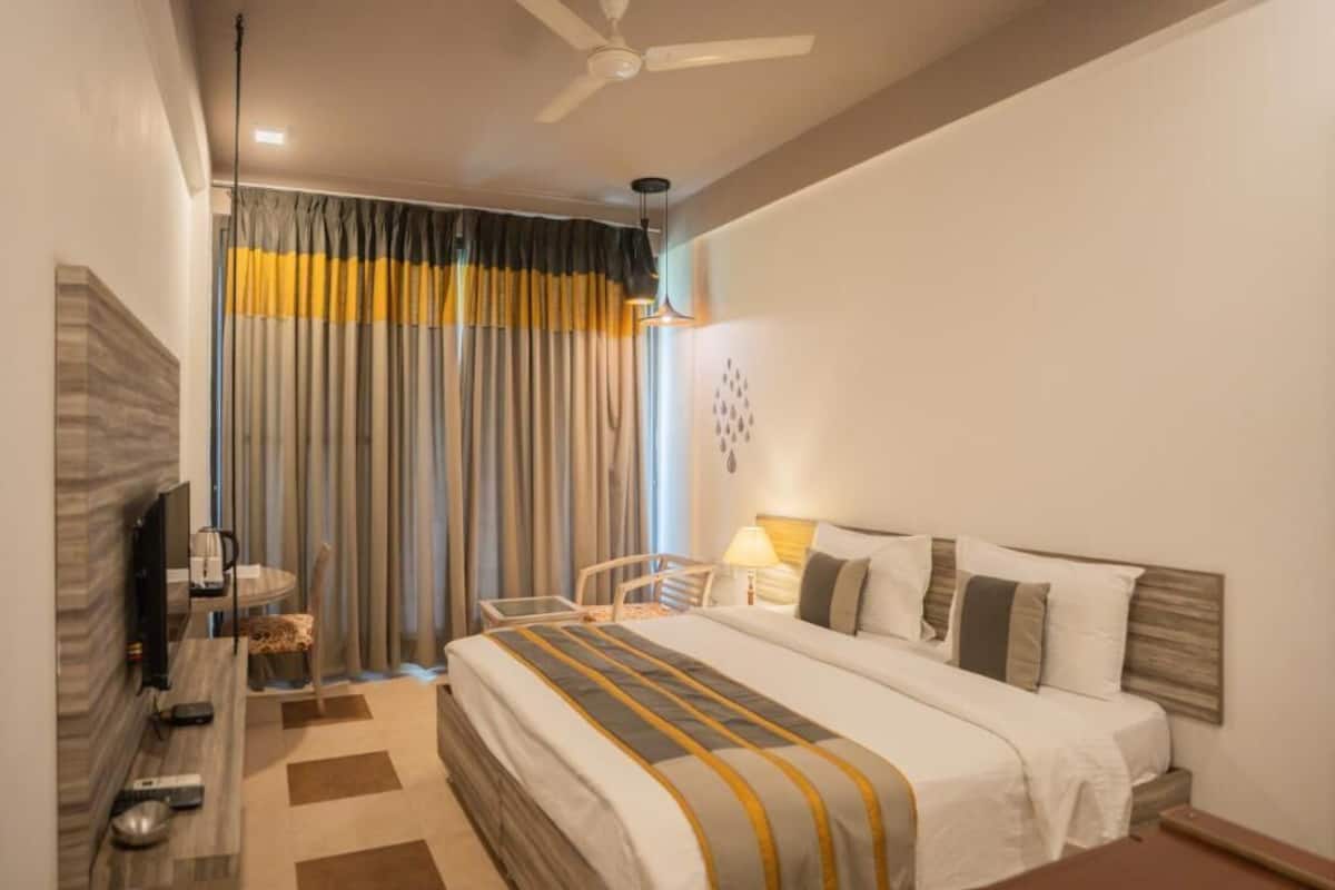 Habitación de hotel con cama, escritorio, silla, televisión y ventilador de techo.