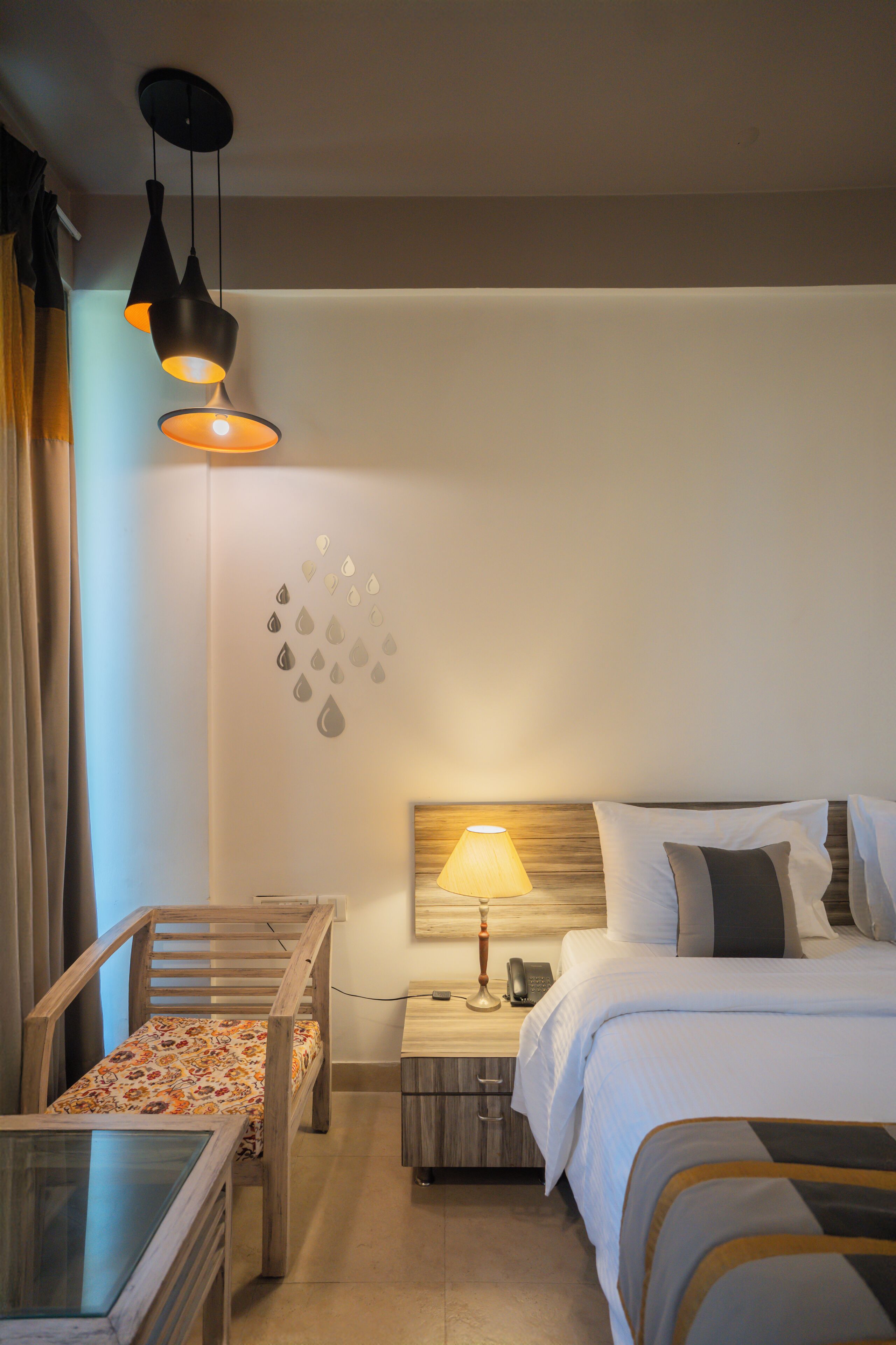 Una habitación de hotel con cama, mesita de noche, lámpara, silla y una pequeña mesa.