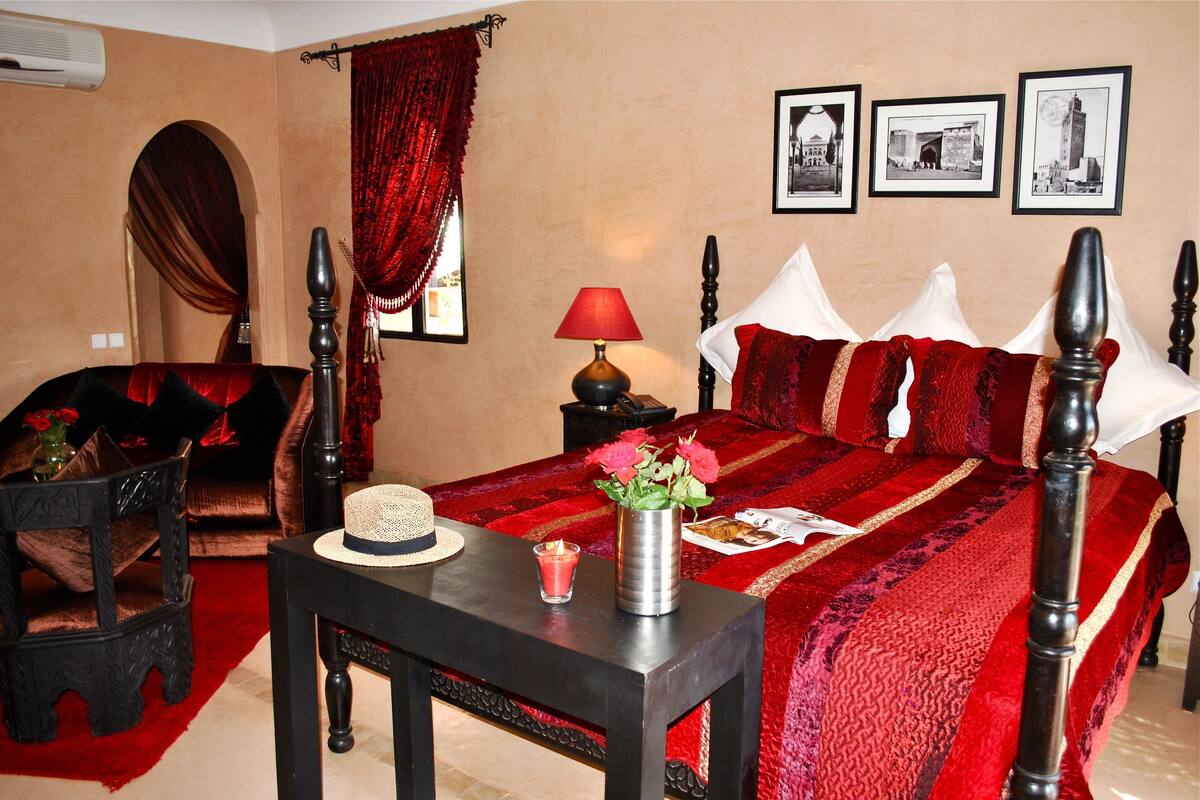 A hotel room with a large bed, a small table with a vase of flowers, a lamp, and a chair.
