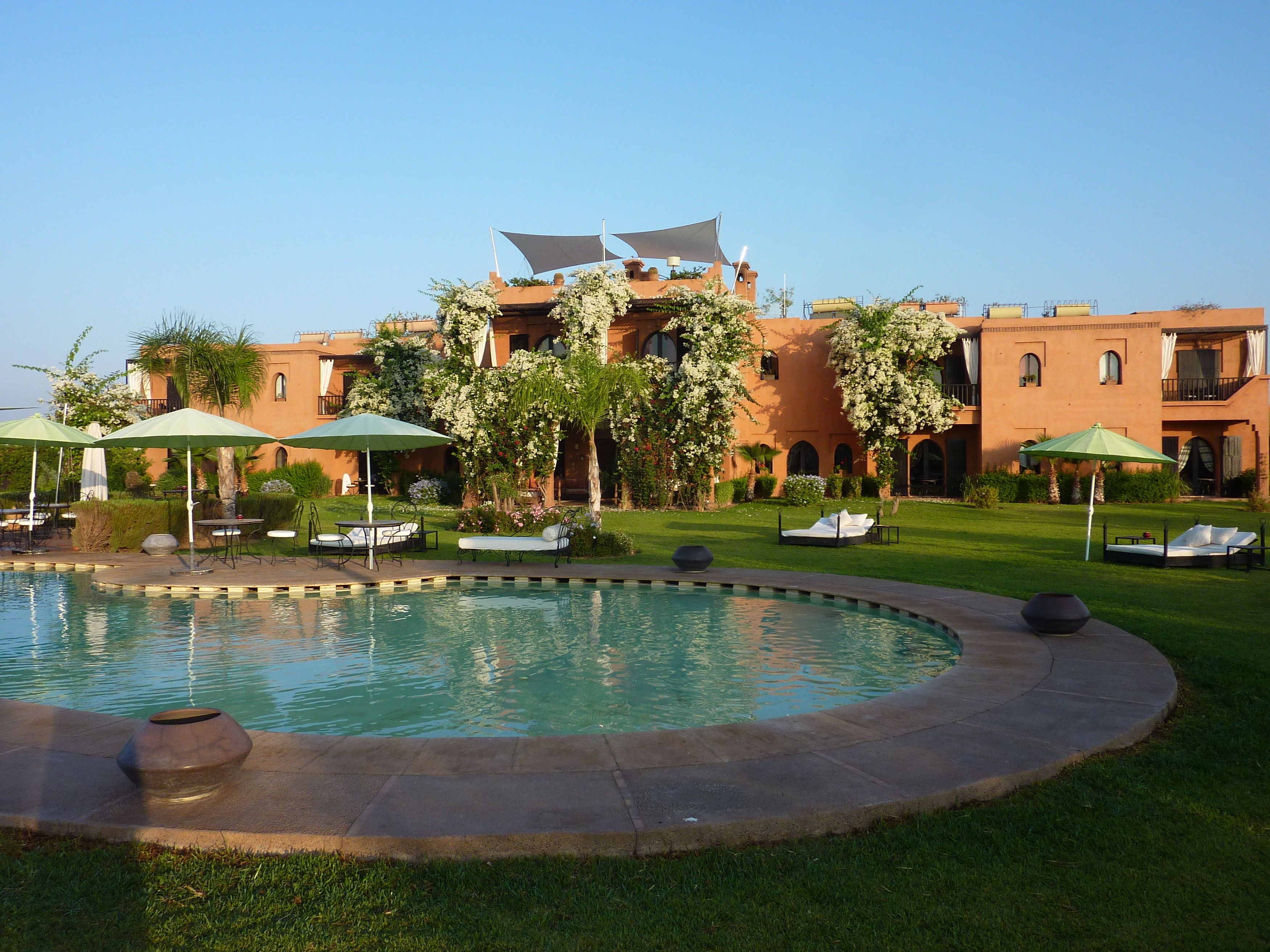 A pool area with lounge chairs and umbrellas, surrounded by well-maintained lawns and flowering plants.