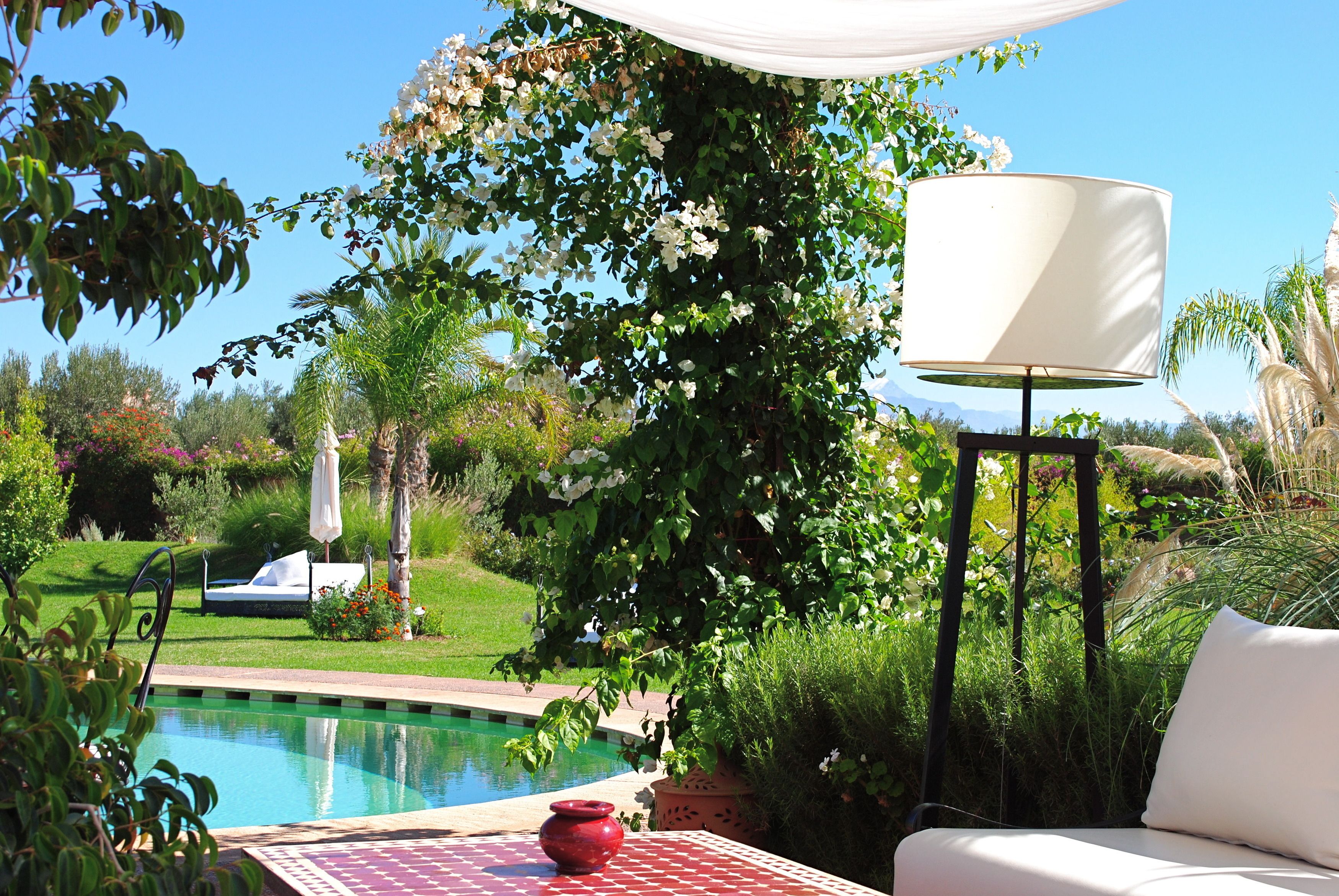 A poolside area with a table, a red vase, and a white lamp.