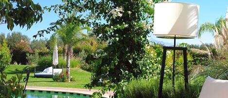 A poolside area with a table, a red vase, and a white lamp.