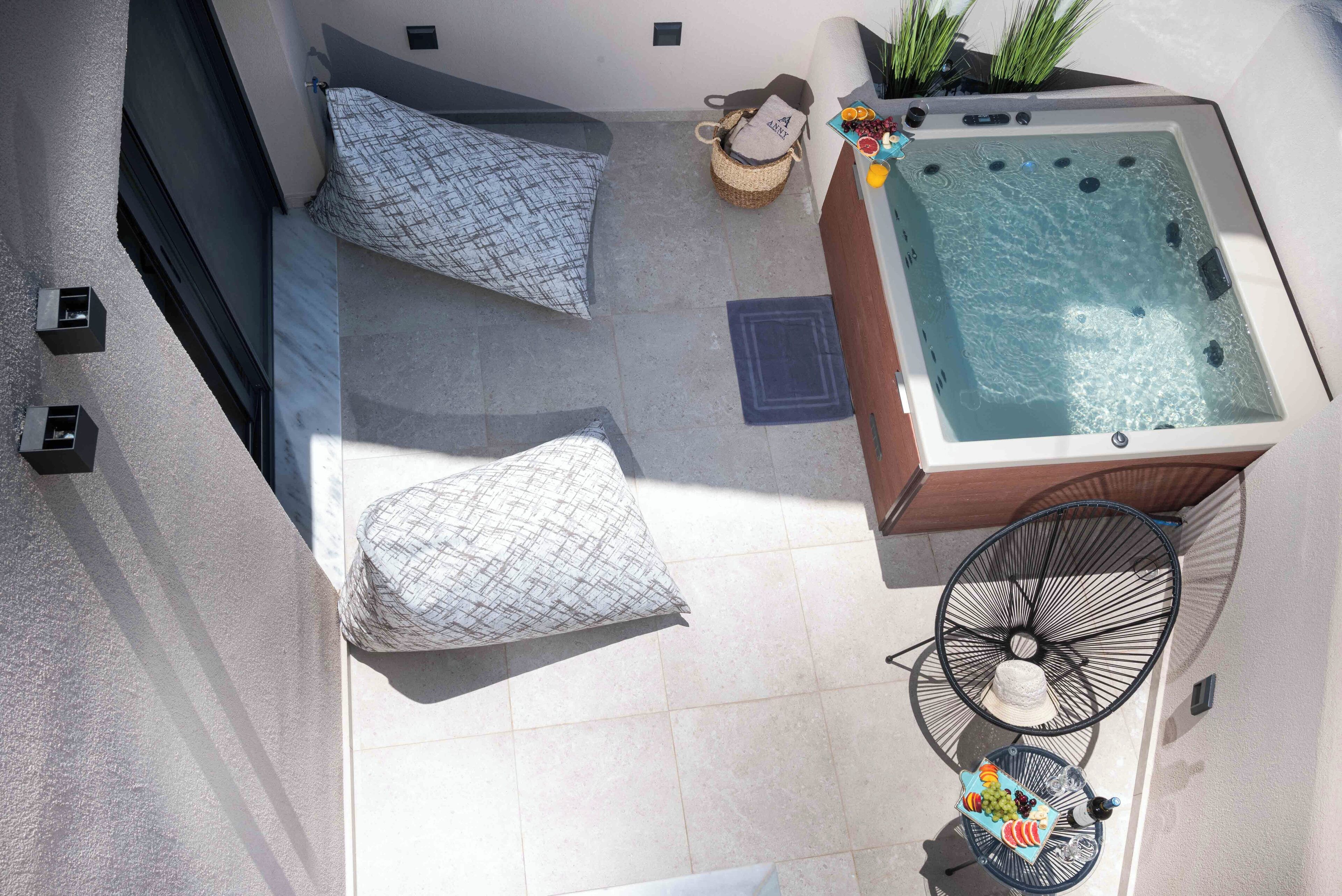 A rooftop terrace with a hot tub, two patterned cushions, a wicker basket, and a table with fruits and a bottle.