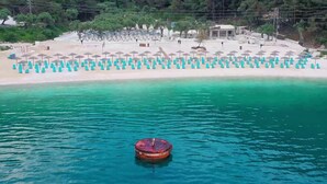 A beach with rows of umbrellas and lounge chairs, a clear turquoise sea, and a small boat in the water. - Anny Residences & Suites (Thasos)