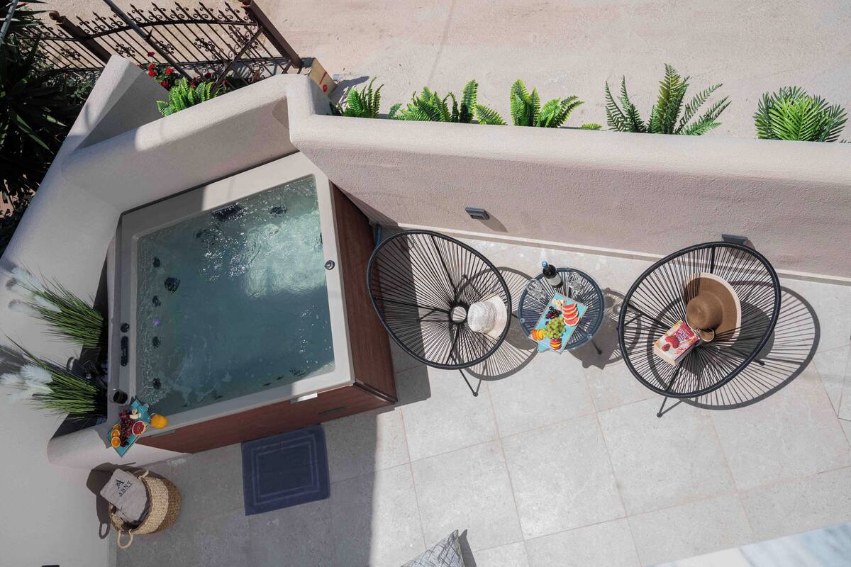 A rooftop pool area with a hot tub, two round tables with umbrellas, and potted plants.