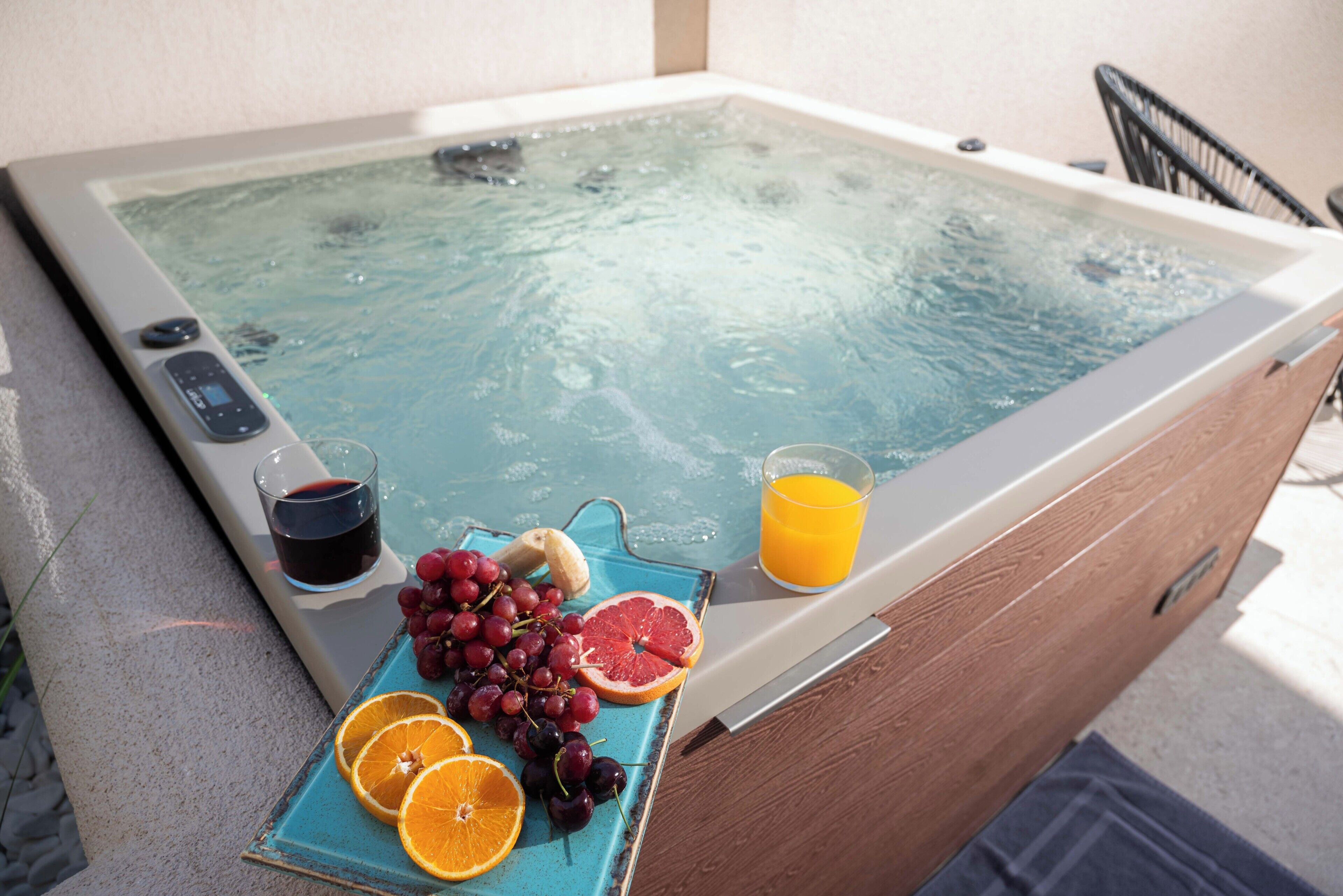 A spa tub with a control panel, a tray with grapes, a grapefruit slice, and a glass of orange juice.