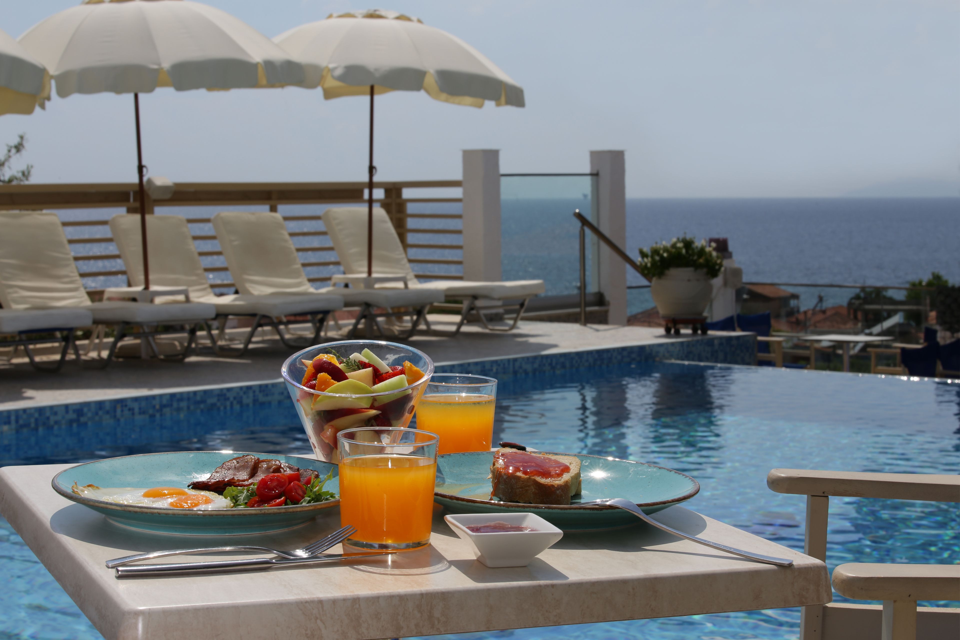 A dining table with a meal, a glass of orange juice, and a view of the ocean.