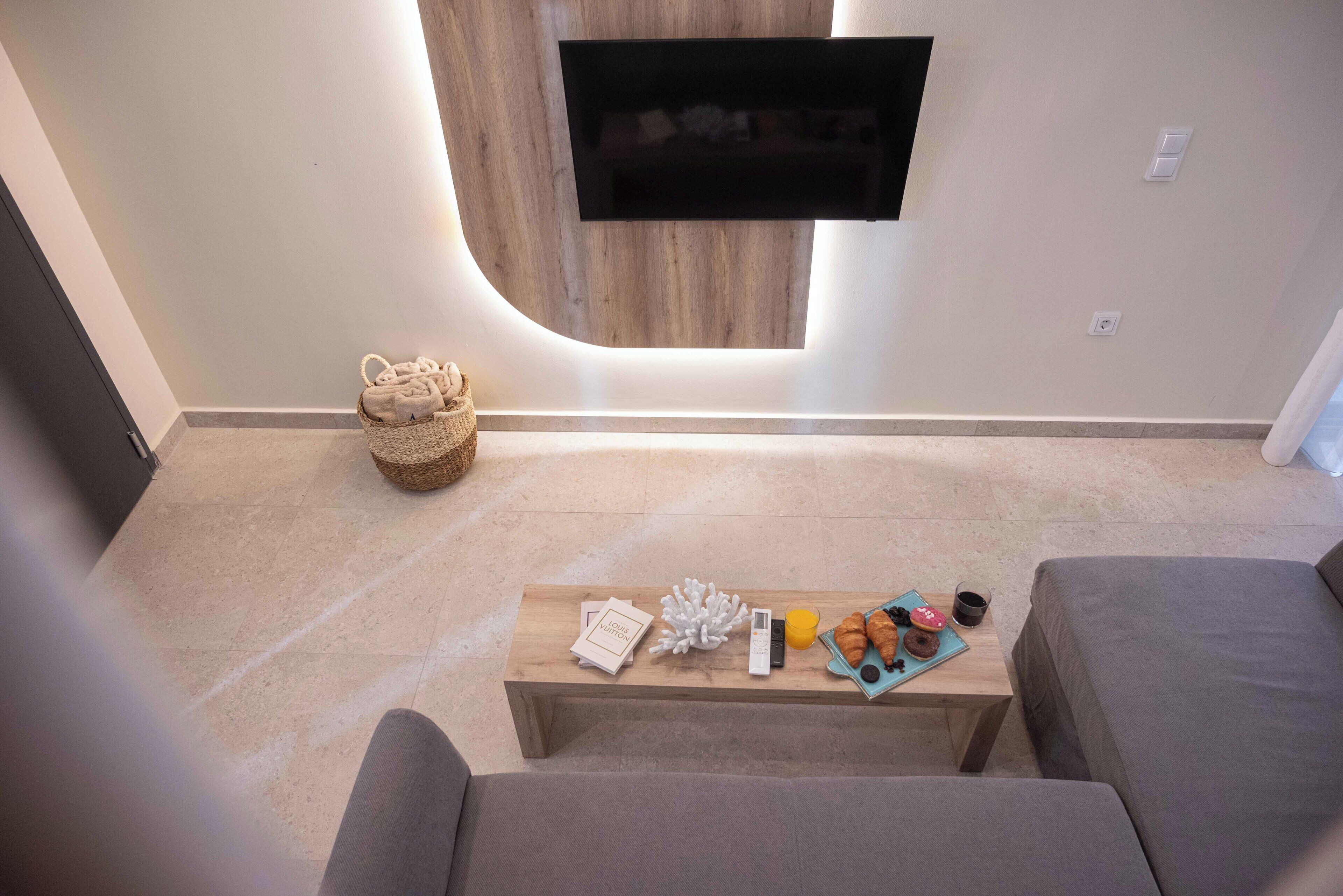 A modern living room with a flat-screen TV mounted on a wooden wall, a coffee table with snacks and a book, and a grey sofa.