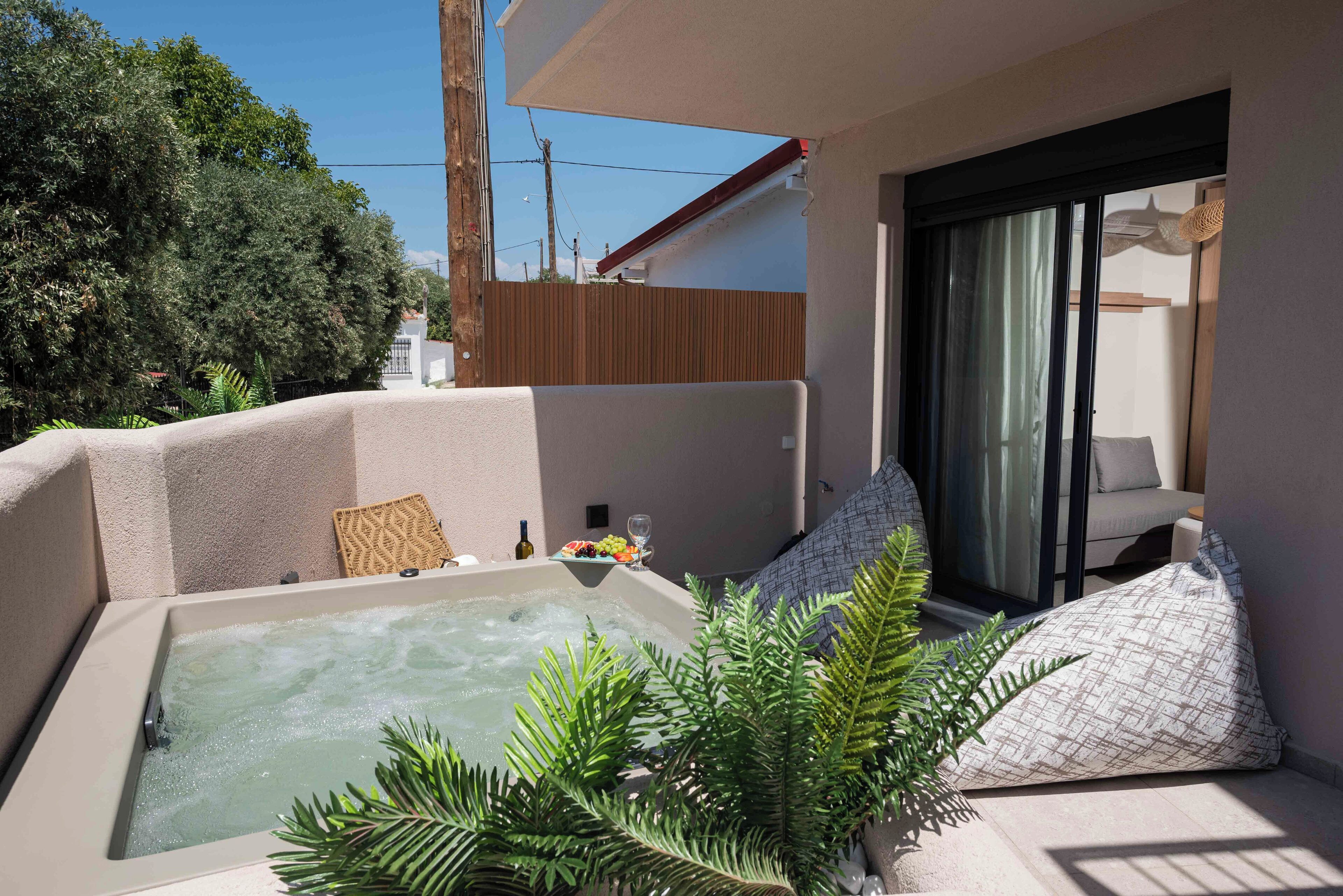 A balcony with a hot tub, a sofa, and a dining table with a glass of wine and fruit.
