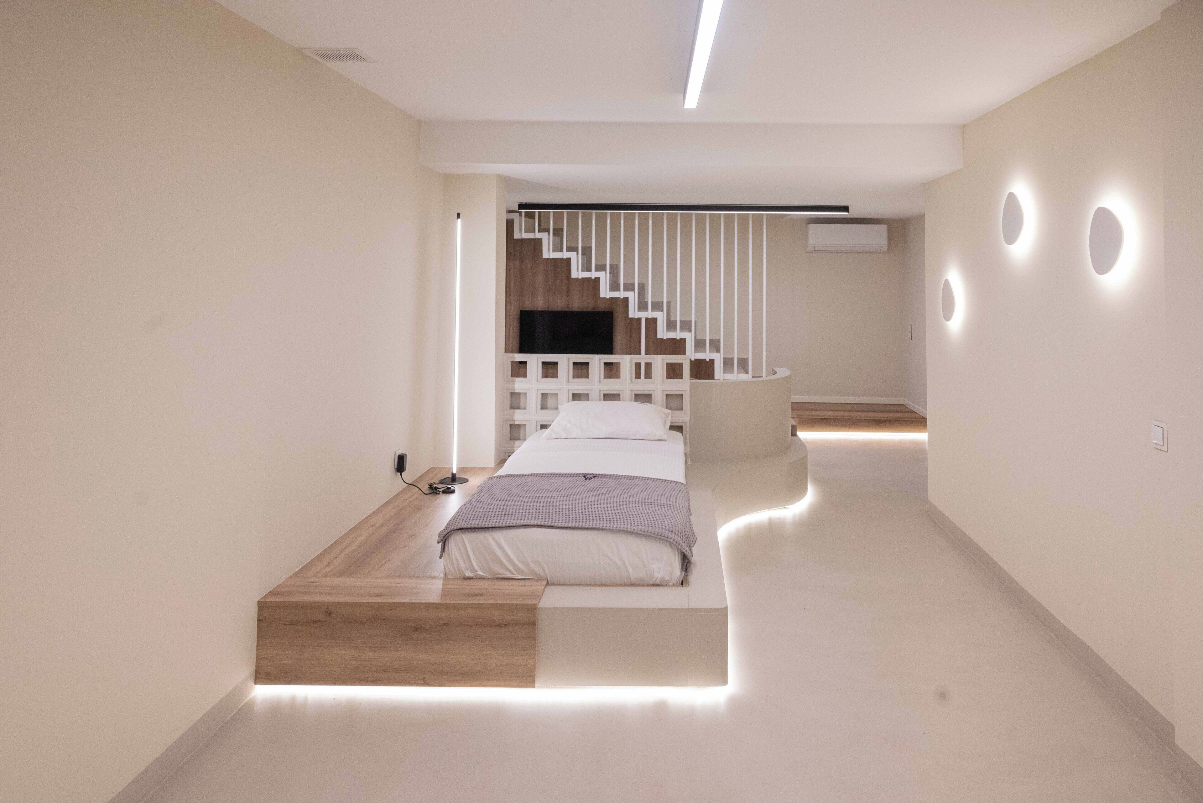 Een moderne slaapkamer met een bed, houten plateau, trap en inbouwverlichting.
