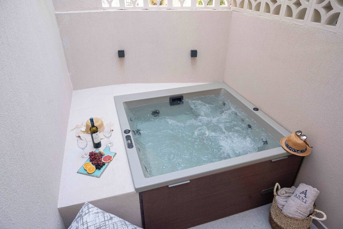 A hot tub with a control panel, a bottle of wine, glasses, and a fruit plate.