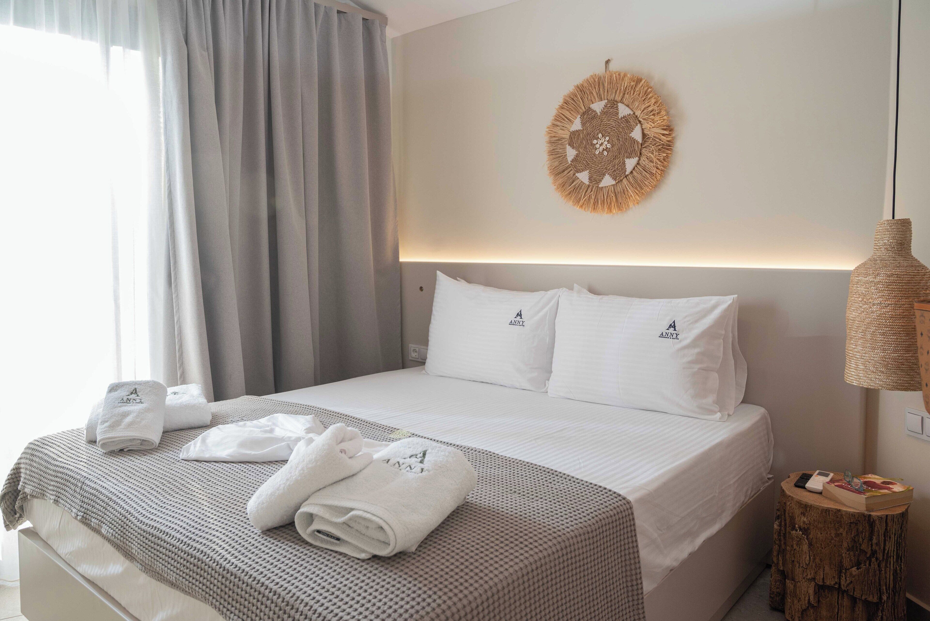 A neatly made bed with a white and gray checkered bedspread, white pillows with a logo, and neatly folded towels on the bed.