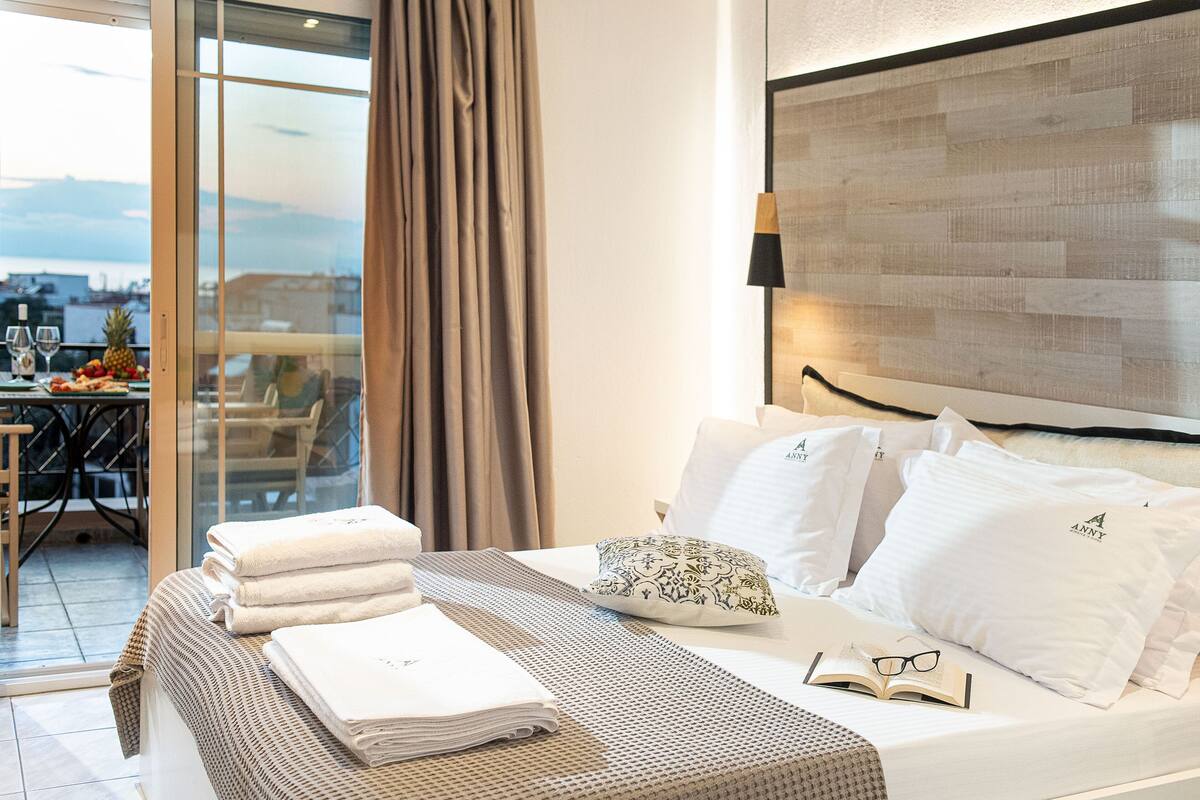 A hotel room with a bed, a view of the city, and a dining area with a table and chairs.