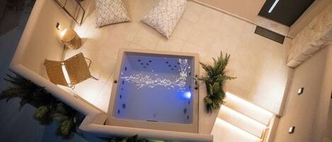 A rooftop jacuzzi with a view of the city, surrounded by lounge chairs and a small table.