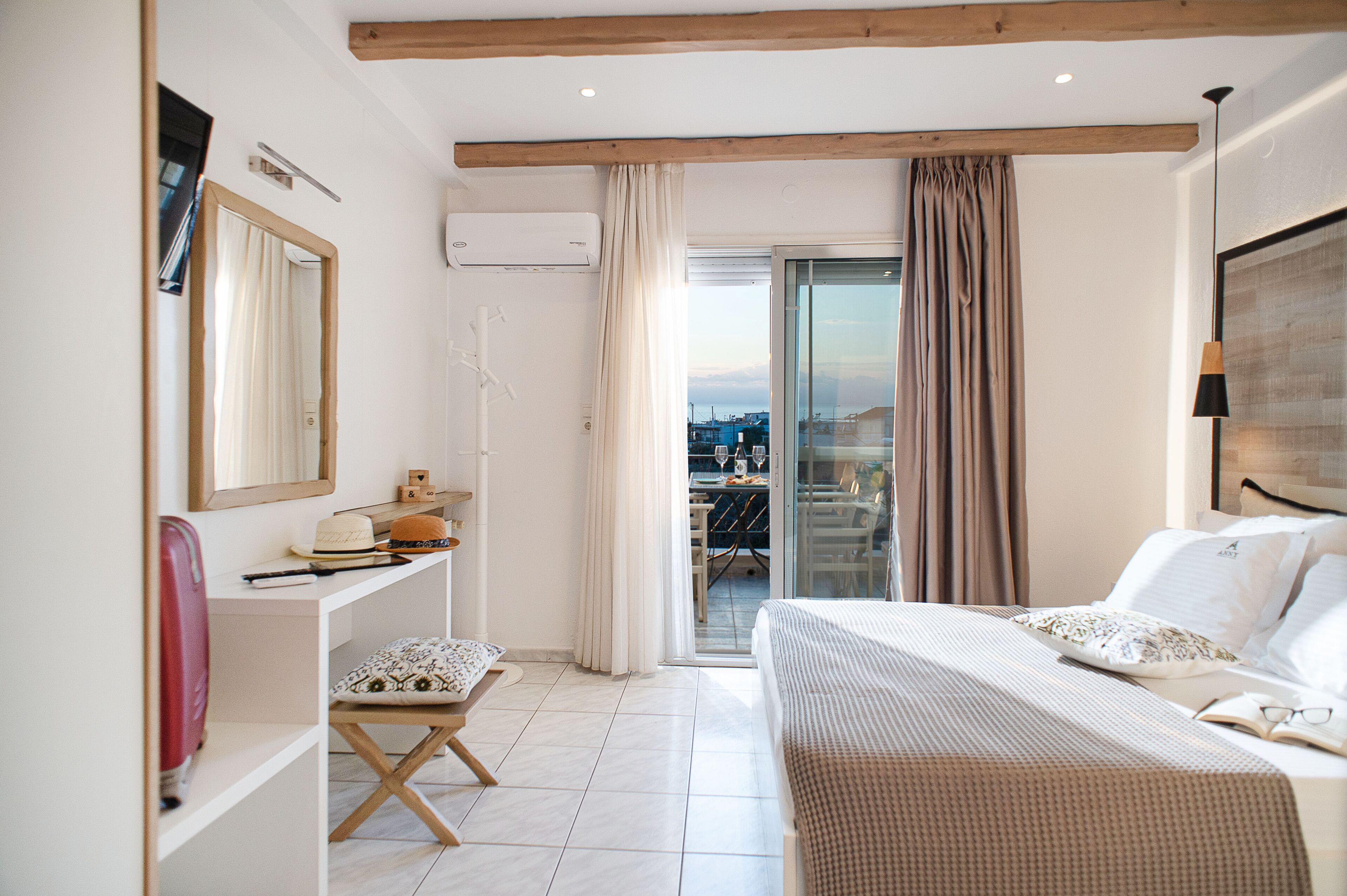 A hotel room with a bed, a desk, a chair, and a view of the city through the balcony.