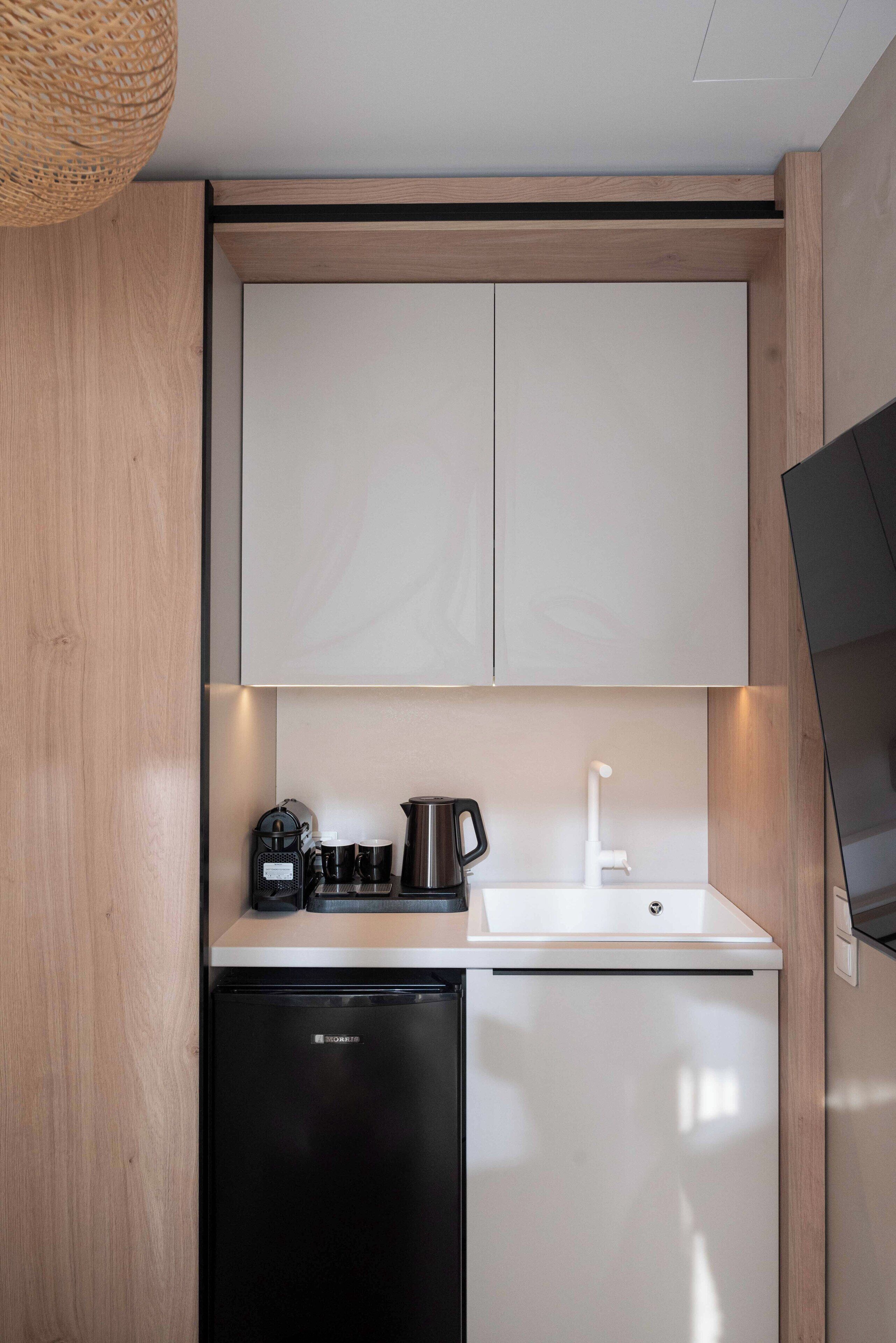 A compact kitchen with white cabinets, a black refrigerator, a coffee maker, and a sink.
