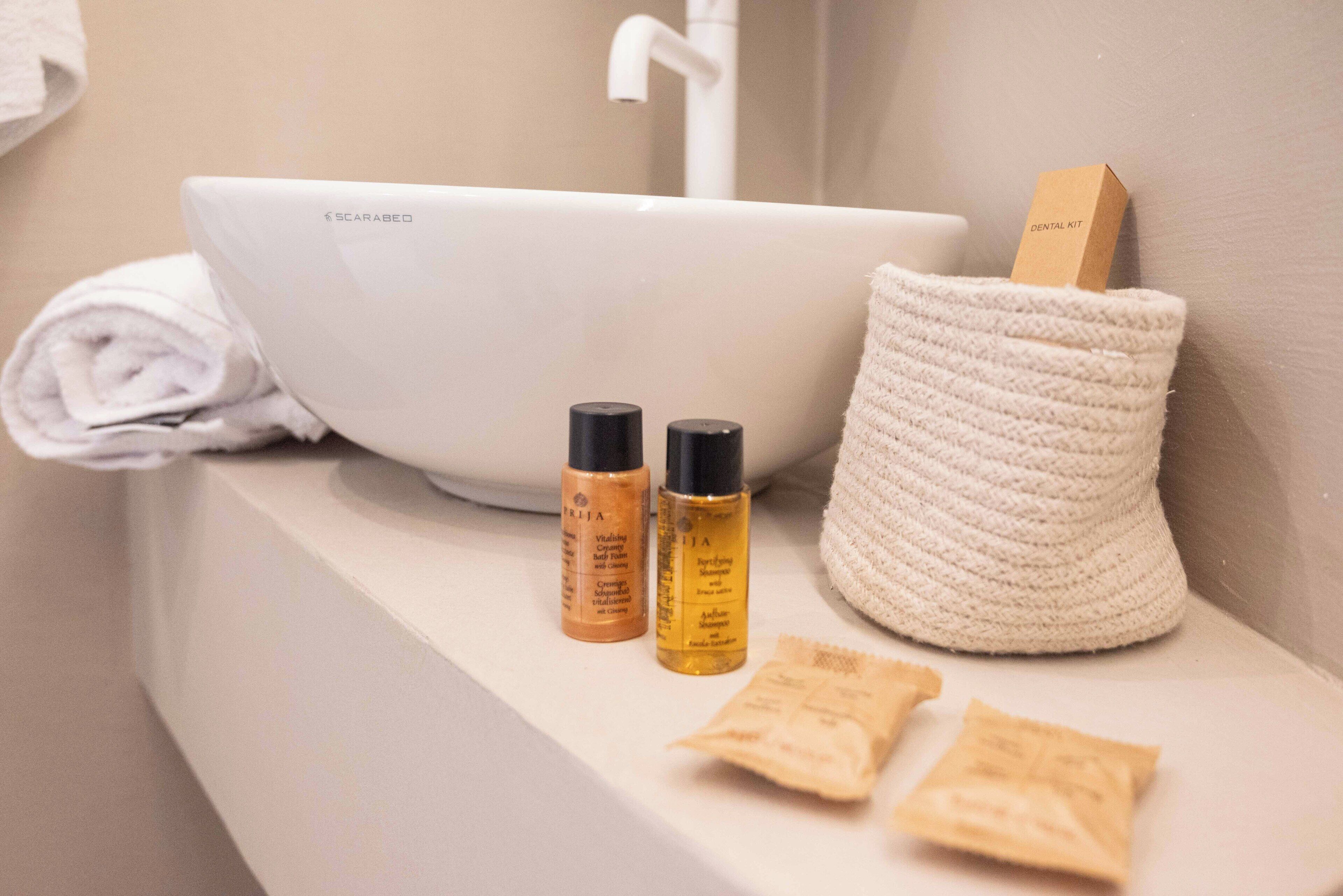 A bathroom sink with a white basin, two skincare bottles, a rolled towel, and a small basket with a box labeled "DENTAL KIT".