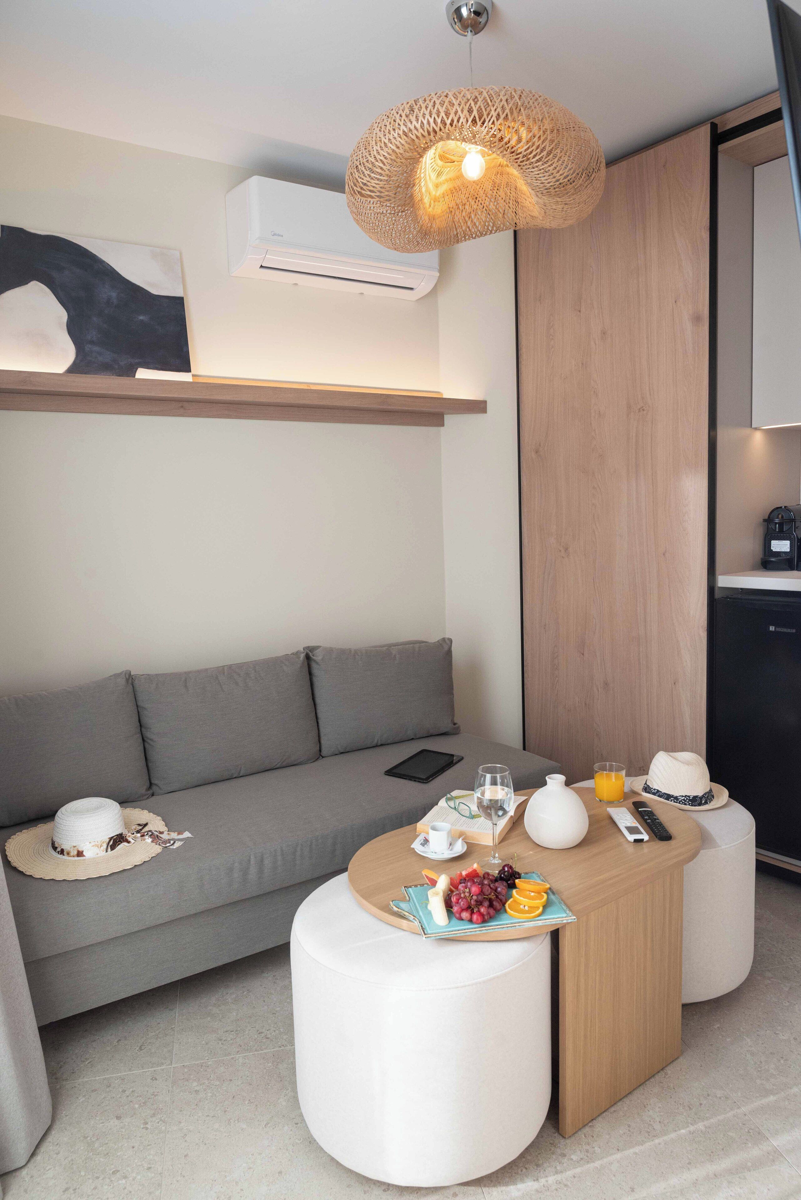 A modern room with a grey sofa, a round wooden table with a white lamp, and a woven light fixture.