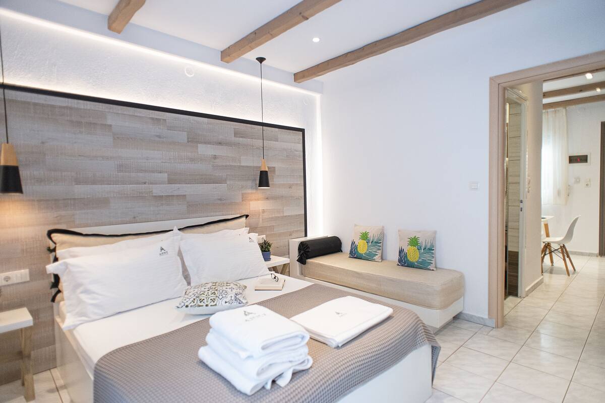 A modern bedroom with a large bed, bedside tables, a bench, and a view of the hallway.